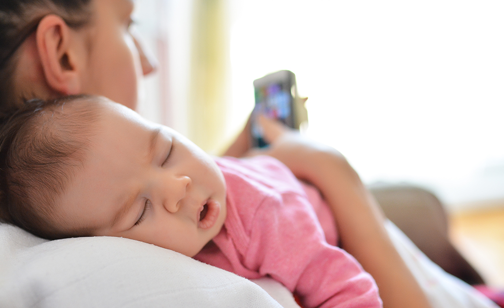 mother looking at her phone with baby resting on her shoulder
